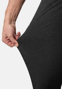 Tirant et étirant un tissu gris foncé de vêtements moulants sur la hanche contre un fond uni.