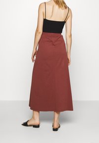 Jupe longue en coton de couleur rouille avec une taille ajustée et un design fluide. Associée à un haut noir à fines bretelles et des sandales noires à enfiler.