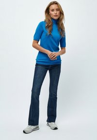 Blå kortärmad polotröja kombinerad med mörkblå utsvängda jeans och grå sneakers. Slät textur och formsytt design.