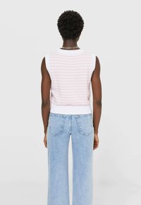 Mouwloze gebreide trui in het wit met een roze patroon, gecombineerd met lichtblauwe hoge taille wijde broek. Heeft geribbelde zoomdetails.
