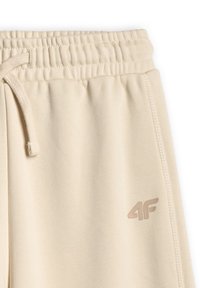 Pantalon de survêtement beige avec taille élastique, cordon, couture latérale et petit logo "4F" près de la poche.