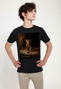 Czarny bawełniany t-shirt z dużą grafiką lwiątka na skalistym tle, z odciskami łap i napisem "Król Lew" na dole.