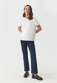 Hvid kortærmet T-shirt med en løs pasform, parret med mørkeblå brede jeans. Sorte loafers fuldender outfittet. Minimalistisk design.