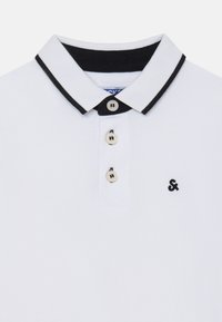 Hvid polo-shirt med sort krave, der har tre knapper og et lille logo på venstre side. Stoffet har en tekstureret overflade.