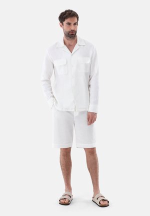 Weißes Leinenhemd mit Kragen und zwei Brusttaschen, kombiniert mit passenden weißen Shorts und beigen Sandalen. Glatte Textur und schlichtes Design.