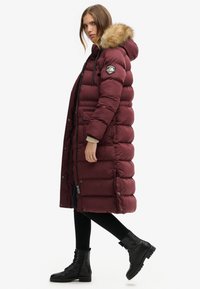 Bordeauxkleurige pufferjas met een capuchon voorzien van nepbont, geribde manchetten, rits- en drukknoopsluiting, zijzakken en een horizontaal gestikte ontwerpen.