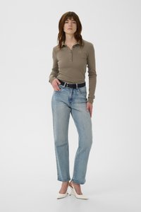 Olivenfarget poloskjorte med lange ermer, kombinert med lys blå jeans med rette ben. Hvite hæler. Enkel design med knappedetaljer og kontrastsøm.