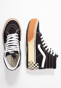 Černé vysoké tenisky s bílými tkaničkami a bočními pruhy. Plátěný materiál, guma na podešvi, vrstvený design a kostkovaný vzor na patě.