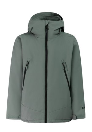 Junge Person trägt einen schwarzen Skihelm, grüne Winterjacke, schwarze Handschuhe, Hose und Stiefel und steht vor neutralem Hintergrund.