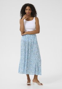 Jupe maxi florale bleu clair avec une taille élastique, assortie à un débardeur blanc et des sandales à talons carrés blanches. Tissu lisse et fluide.