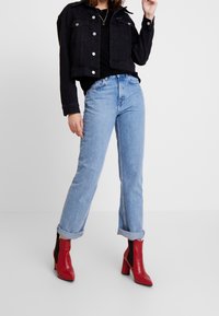 Svart kort denimjacka med silverknappar, i kombination med ljusblå uppvikta jeans och röda klackboots med blockklack.