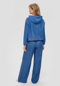 Blauwe chambray trainingsoutfit met een hoodie-jack en wijde pantalons. Heeft elastische manchetten en een textuurstof. Eenvoudig, ontspannen pasvorm ontwerp.