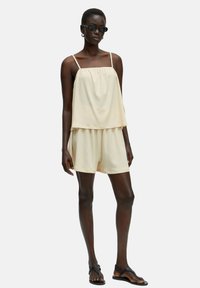 Lichtbeige tweedelig outfit bestaande uit een losse, gelaagde top en bijpassende korte broek in textuurstof, met dunne bandjes en een relaxte pasvorm.