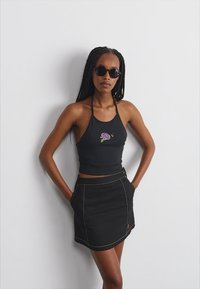 Top nero a fascia con dettaglio di ricamo floreale abbinato a una mini gonna in denim nera con cuciture a contrasto e tasche laterali.