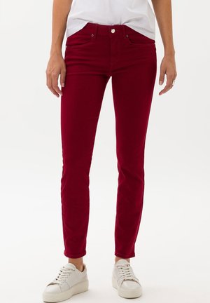Röda, tight passande jeans med en slät textur, fem fickor och knäppning, som är parat med vita sneakers för en avslappnad look.