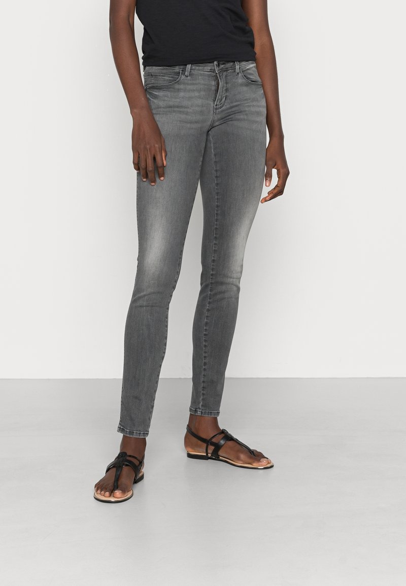 Jeans skinny grises de denim, con un diseño desgastado y una cintura de altura media, combinados con sandalias negras de tiras.