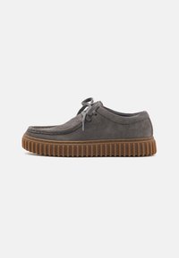 Gray suede shoe with a rounded toe, lace-up design, and a thick, ridged brown rubber sole. Smooth texture with minimal stitching details.