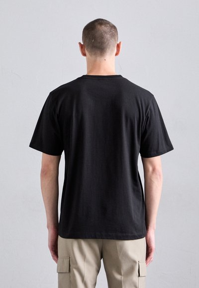T-shirt en coton noir à manches courtes, col rond et coupe ample. Texture visible avec une surface lisse et un minimum de détails de couture à l'arrière.