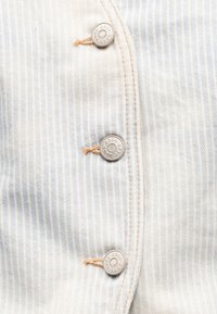 Tissu rayé bleu clair et blanc avec trois boutons en métal portant l'inscription "BOSS" et couture avec un fil orange.