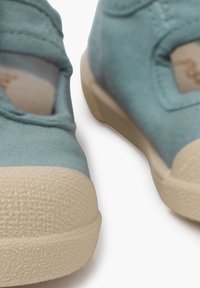 Helle blaue Leinenschuhe mit abgerundeten Zehen, strukturierten beigen Gummisohlen und seitlichen Ausschnitten zur Belüftung. Saubere Nähte sichtbar.