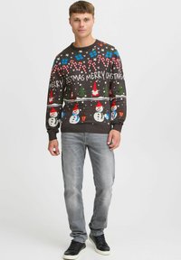 Stickad jultröja med snögubbar, godiskäppar och träd i röd, grön och blå på en mörk bakgrund. Ribbad mudd och nederkant.