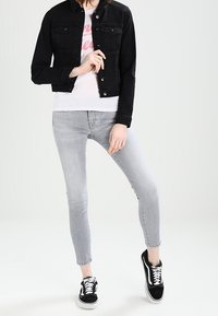 Black denim jacket, white t-shirt with pink text, gray skinny jeans, and black sneakers. Smooth materials with contrasting colors and casual fit.