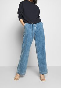 Navy texturerad sweatshirt ihop med vida ljusblå jeansbyxor. Byxorna har dragsko i midjan och rak nederkant. Neutrala öppna sandaler.