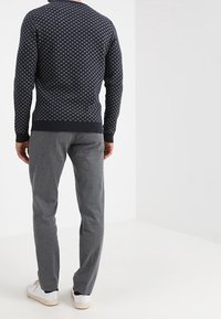 Navy patterned sweater with a round neck, paired with light gray textured pants and white sneakers, viewed from the back.