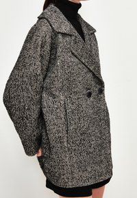 Hahnentrittmuster Übermantel in Schwarz und Weiß, mit einem breiten Kragen, zwei frontalen Taschen und doppelter Knopfverschluss.