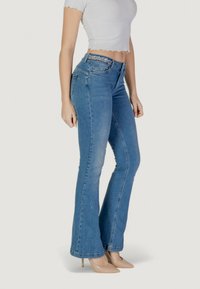 Jeans a zampa d'elefante in denim blu con vita alta, caratterizzati da una cintura testurizzata e dettagli di cucitura. Abbinati a tacchi a punta beige.