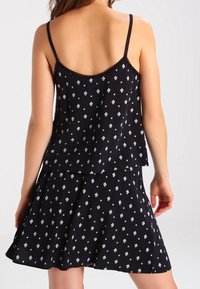 Abito nero senza maniche con design a strati, caratterizzato da un motivo geometrico bianco e una silhouette fluida. Spalline regolabili.