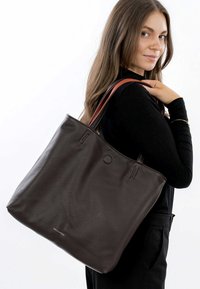 Brun læder tote taske med struktureret overflade, der har korte håndtag i en kontrastfarve af tan, og et minimalistisk logo på forsiden.