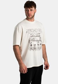 Camiseta de gran tamaño en color crema que presenta un diseño de arte en línea negra de una escena de bar con el texto "PEGADOR. Aroma a verano." Manga corta, material de algodón.