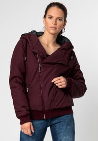 Burgundy puffer jacket with large hood, zippered front, and ribbed cuffs. Features side pockets and a smooth, textured exterior.