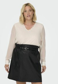 Lys, let bluse med prikkede mønstre og blonder, parret med en sort faux læder nederdel med bæltestrop og sidelommer.