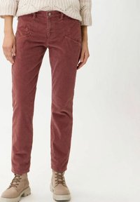 Pantalon en velours côtelé rouge à coupe ajustée, doté de poches avant, de fines rainures et d'une fermeture à bouton, associé à des bottes beiges à lacets.