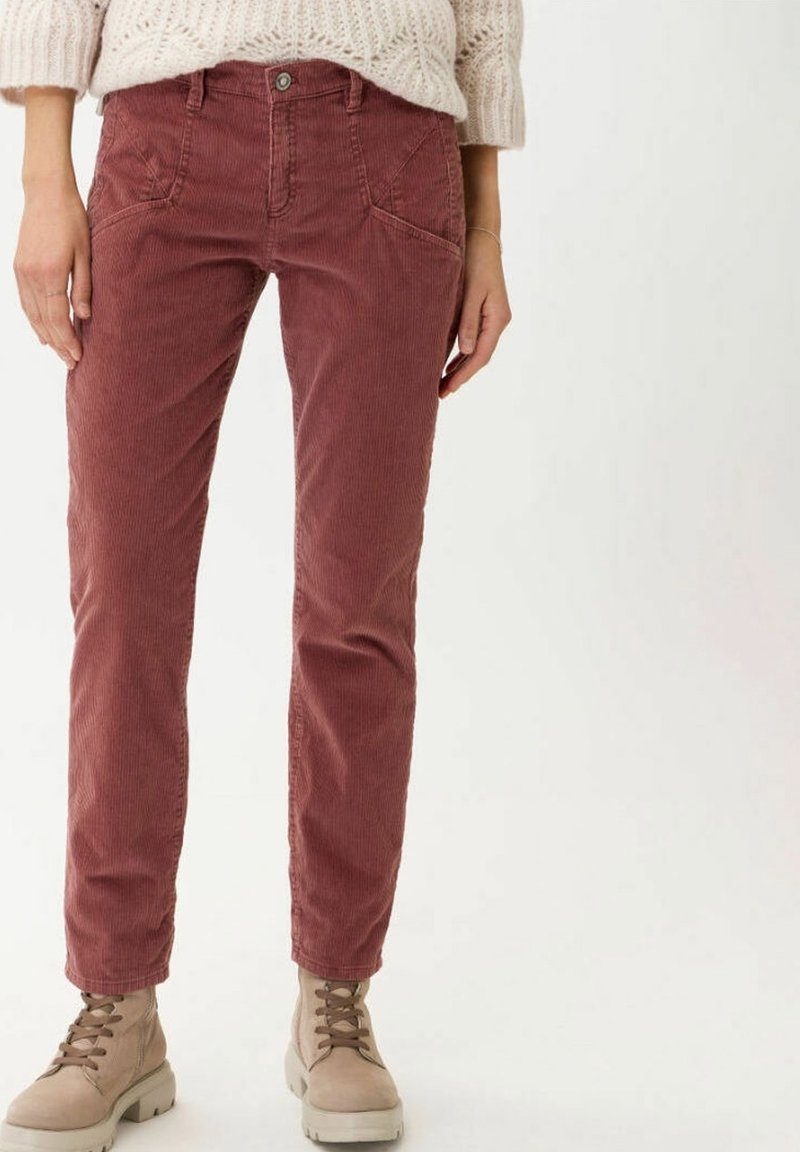 Pantalon en velours côtelé rouge à coupe ajustée, doté de poches avant, de fines rainures et d'une fermeture à bouton, associé à des bottes beiges à lacets.
