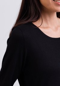 Schwarzes langärmliges Top mit rundem Ausschnitt, aus feinem Strickstoff mit glatter Textur und subtiler Eleganz.