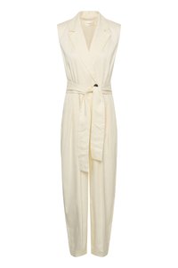 Combinaison crème sans manches avec col à revers, taille ceinturée et pantalon tailleur longueur totale.