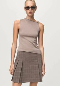 Top sans manches ajusté brun clair avec un col légèrement asymétrique, associé à une jupe plissée en tartan brun. Tissu texturé et lisse.