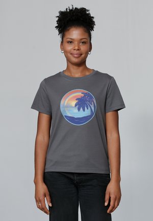 T-shirt en coton gris avec un graphique circulaire représentant un coucher de soleil sur une plage et un palmier dans des couleurs pastel. Manches courtes, col ras du cou.