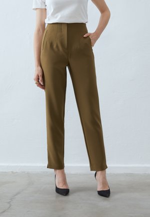 Brune høy midje bukser med skreddersydde folder og sidelommer, parret med svarte hæler. Jevn tekstur, slim fit, ankellengde design.