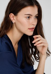 Boucles d'oreilles en argent avec un design circulaire, présentant une texture lisse et épurée ainsi qu'un style minimaliste. Portées par un mannequin avec de longs cheveux ondulés.