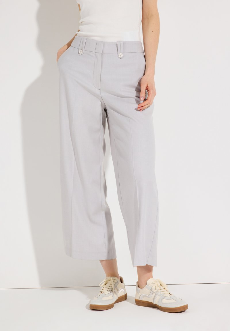 Person wearing light gray wide-leg cropped pants with front buttons and white sneakers, standing against a plain white background.