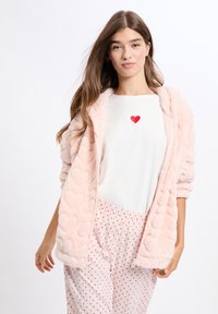 Różowa, miękka bluza na zamek z motywem serduszek, noszona na białej bluzce z małym czerwonym sercem. Do tego wzorzyste spodnie od piżamy.