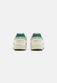 Sneakers z beżowym korpusem, zielonymi akcentami i białymi detalami. Z tyłu znajdują się napisy "1973" w kolorze szarym. Wykonane ze skóry i zamszu. Płaskie podeszwy.