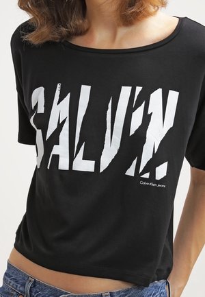 Black short-sleeve t-shirt with a large white graphic print reading "CALVIN" and a smaller "Calvin Klein Jeans" logo on the front.