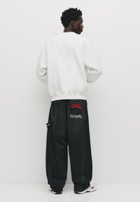 Løse sorte jeans med røde og hvide grafiske detaljer på lommerne, parret med en hvid crewneck sweatshirt. Har en afslappet pasform.