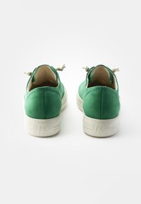 Grüne Wildleder-Sneaker mit weißen Gummisohlen, die strukturierte Akzente und dekorative Schnürsenkel an der Ferse aufweisen. Auffälliges Logo auf der Sohle.