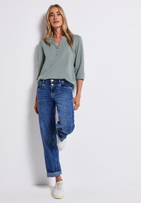 Camicetta henley verde chiaro a tre quarti, abbinata a jeans blue denim comodi. Sneakers bianche completano l'outfit casual.